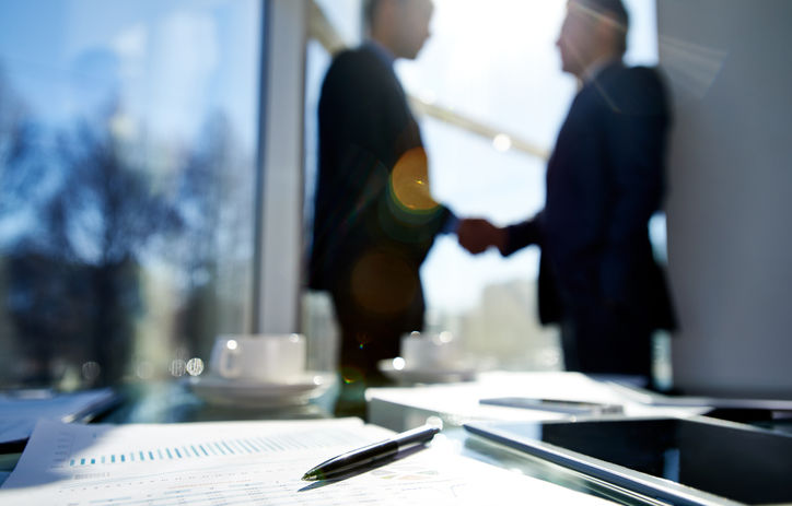 Financial report, pen and tablet computer on the desk Financial report, pen and tablet computer on the desk, two businessmen shaking hands in the background